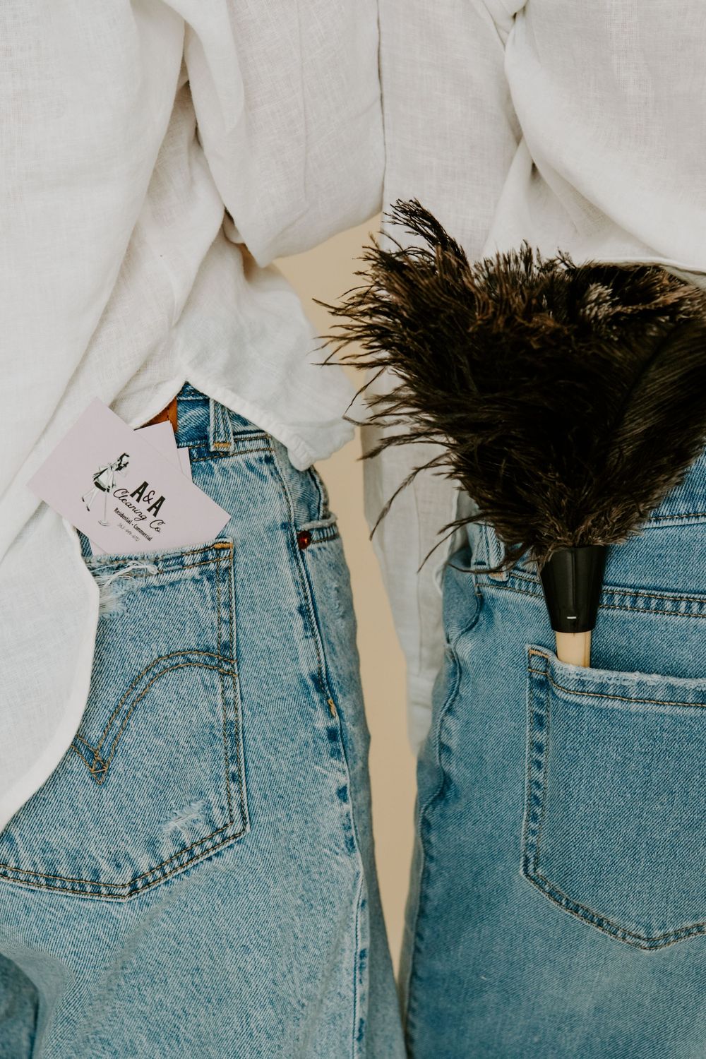 Two people in light wash Levi's jeans with white shirts, one holding a business card and other a feather duster.