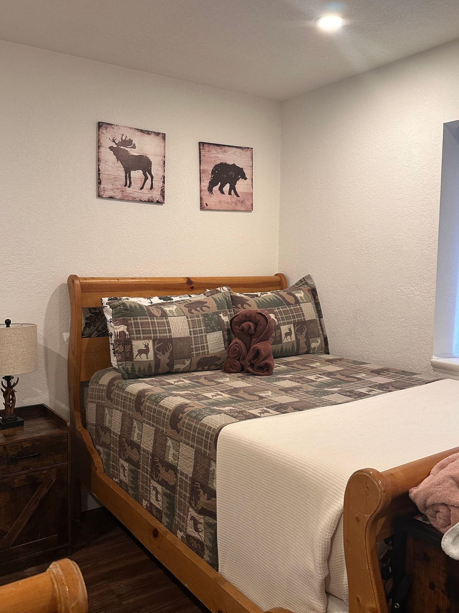 Rustic bedroom with sleigh bed, plaid wildlife bedding, moose and bear wall art, and warm wood nightstand.