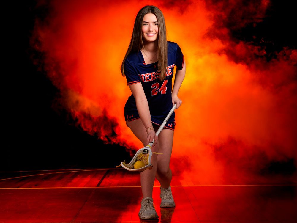 Hershey Lacrosse senior #24 poses with stick against orange smoke, Media Day by Deanna Fox, SportsFox Photography based in Hershey PA