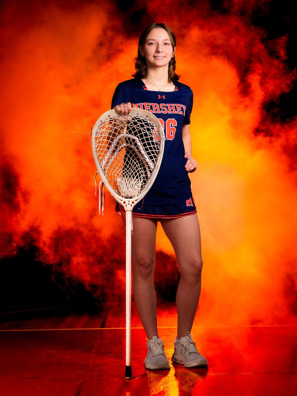 Hershey Lacrosse senior poses with stick and net in orange smoke, Media Day by Deanna Fox, SportsFox Photography based in Hershey PA