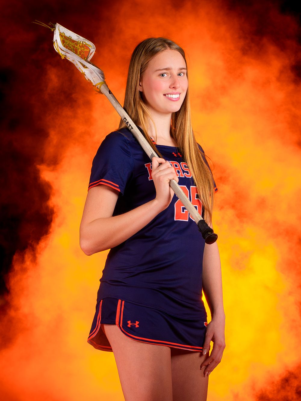 Hershey Lacrosse senior poses with stick over shoulder in orange smoke, Media Day by Deanna Fox, SportsFox Photography based in Hershey PA