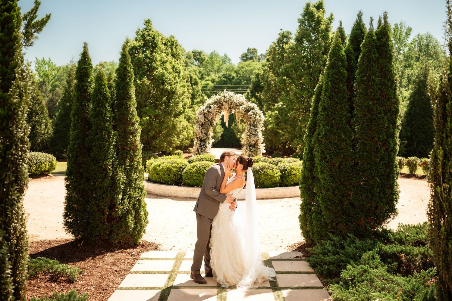 Happy couple embracing outdoors near red tulips, smiling and wearing white shirts in a romantic garden setting.