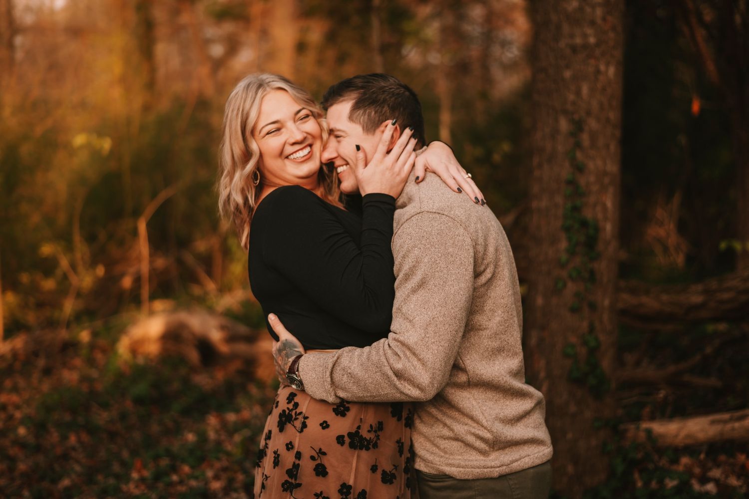 A couple embraces and laughs together in a sunlit autumn forest during an engagement photo session.