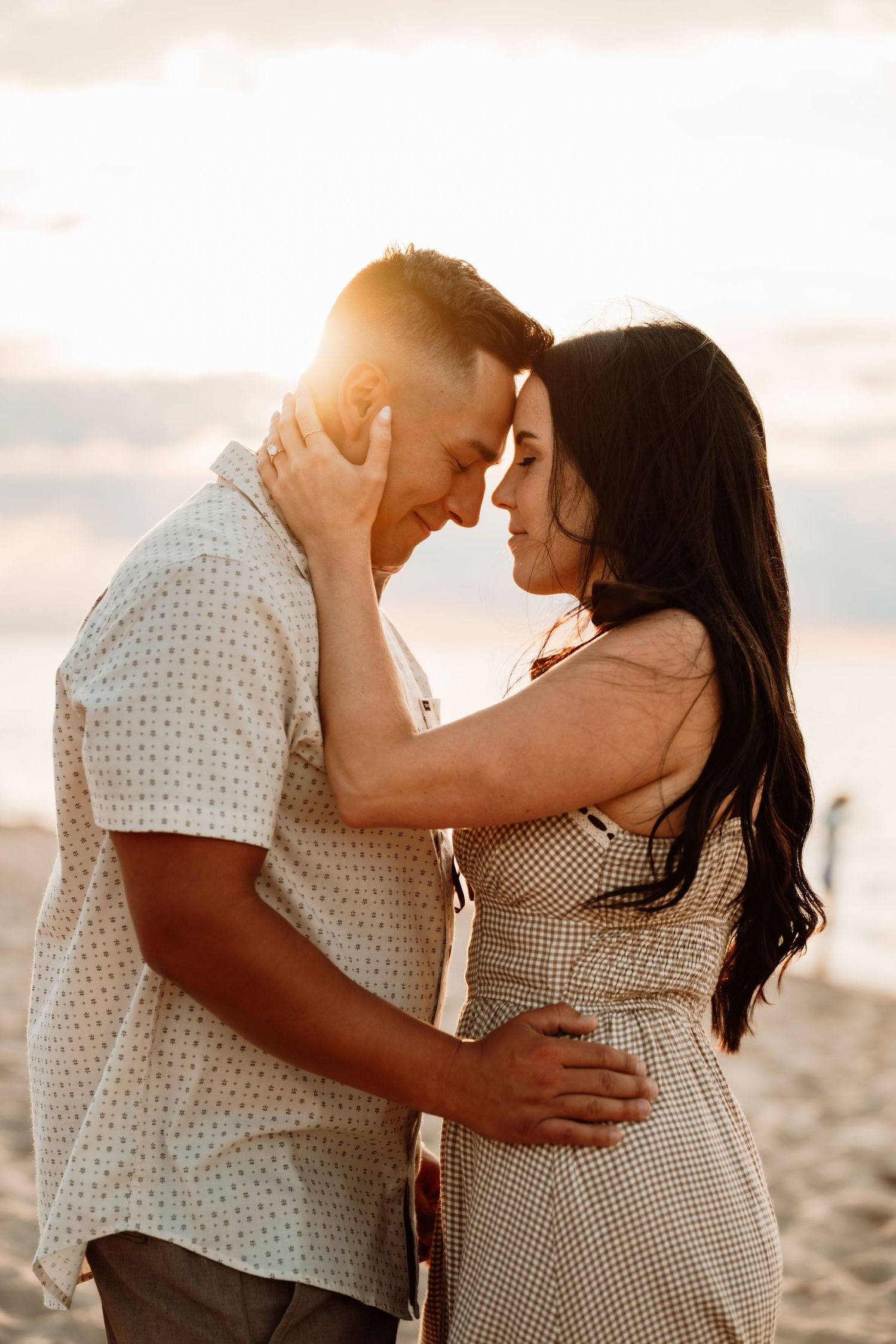 A couple shares a romantic sunset moment on the beach, foreheads touching, bathed in golden light.