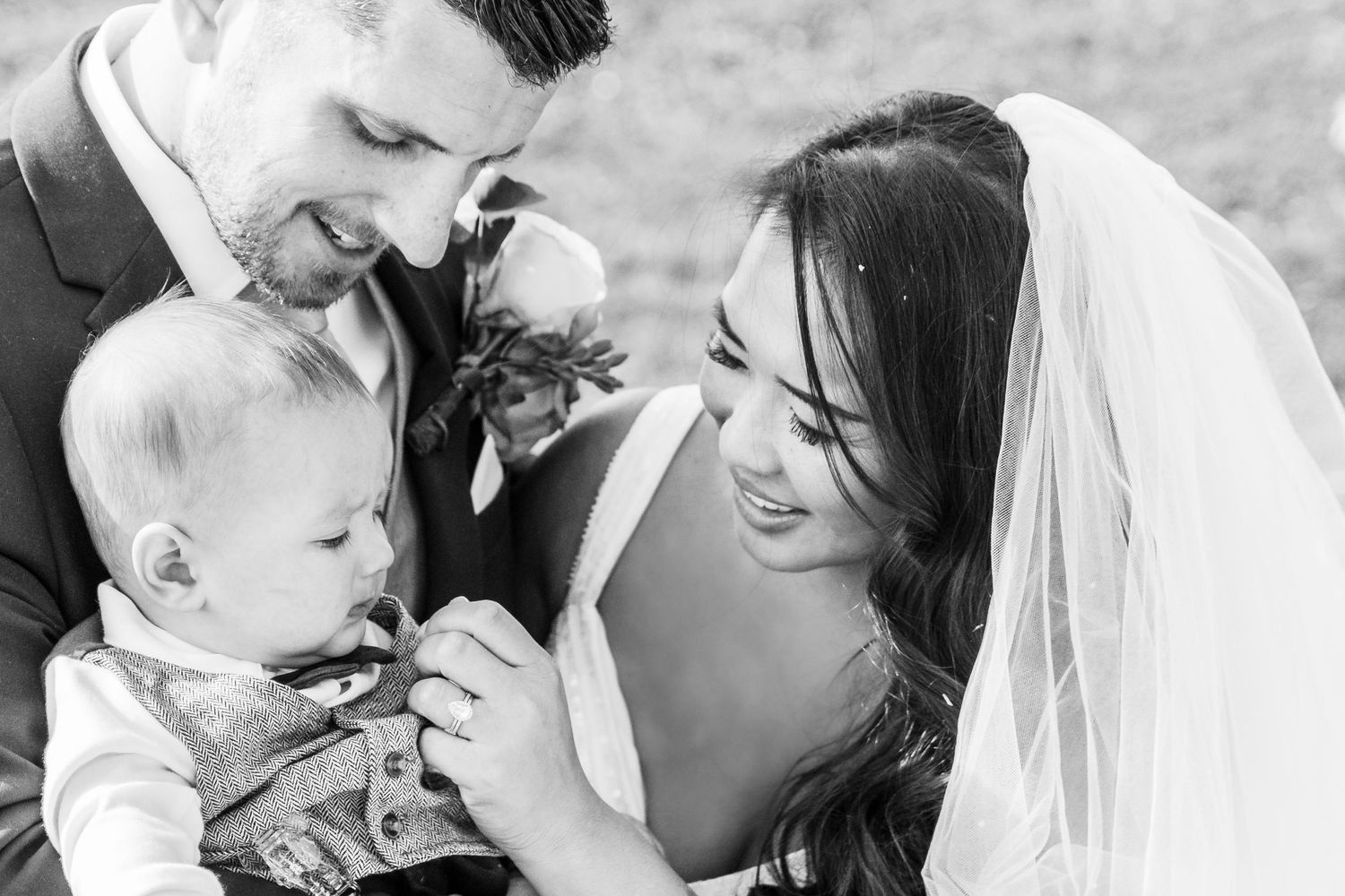 Bride and groom pose with two French Bulldogs under a stunning purple wisteria arch at their outdoor wedding.