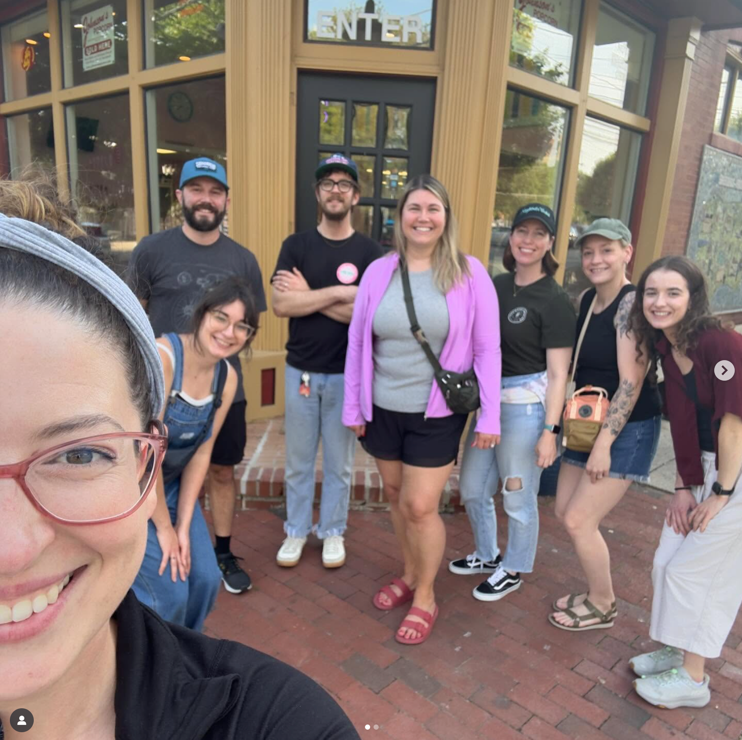 People stand in front of a wooden building entrance with double doors in a casual group setting.