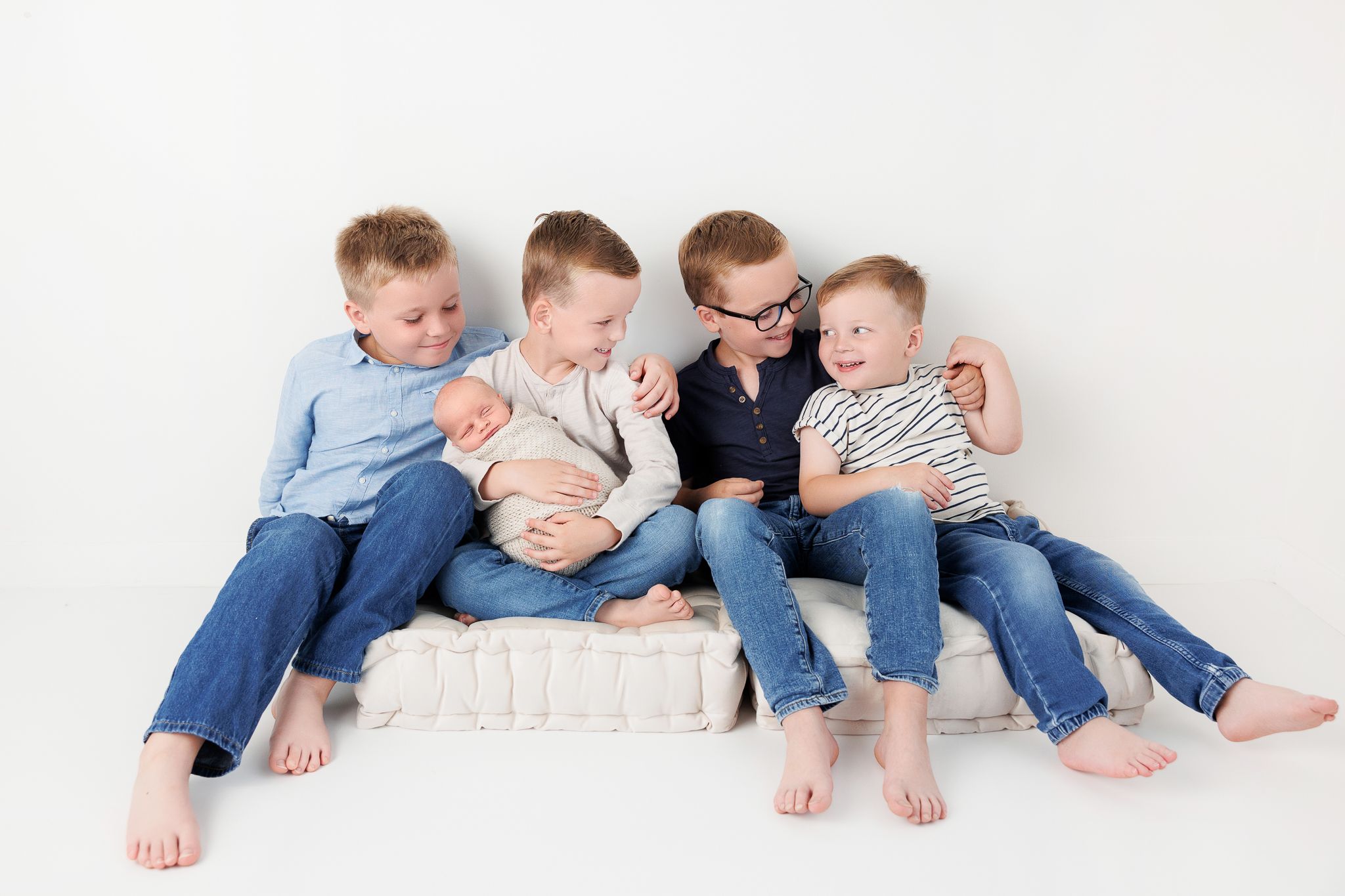 Four young boys in matching blue and white outfits sit together in a line showing their bare feet and legs.