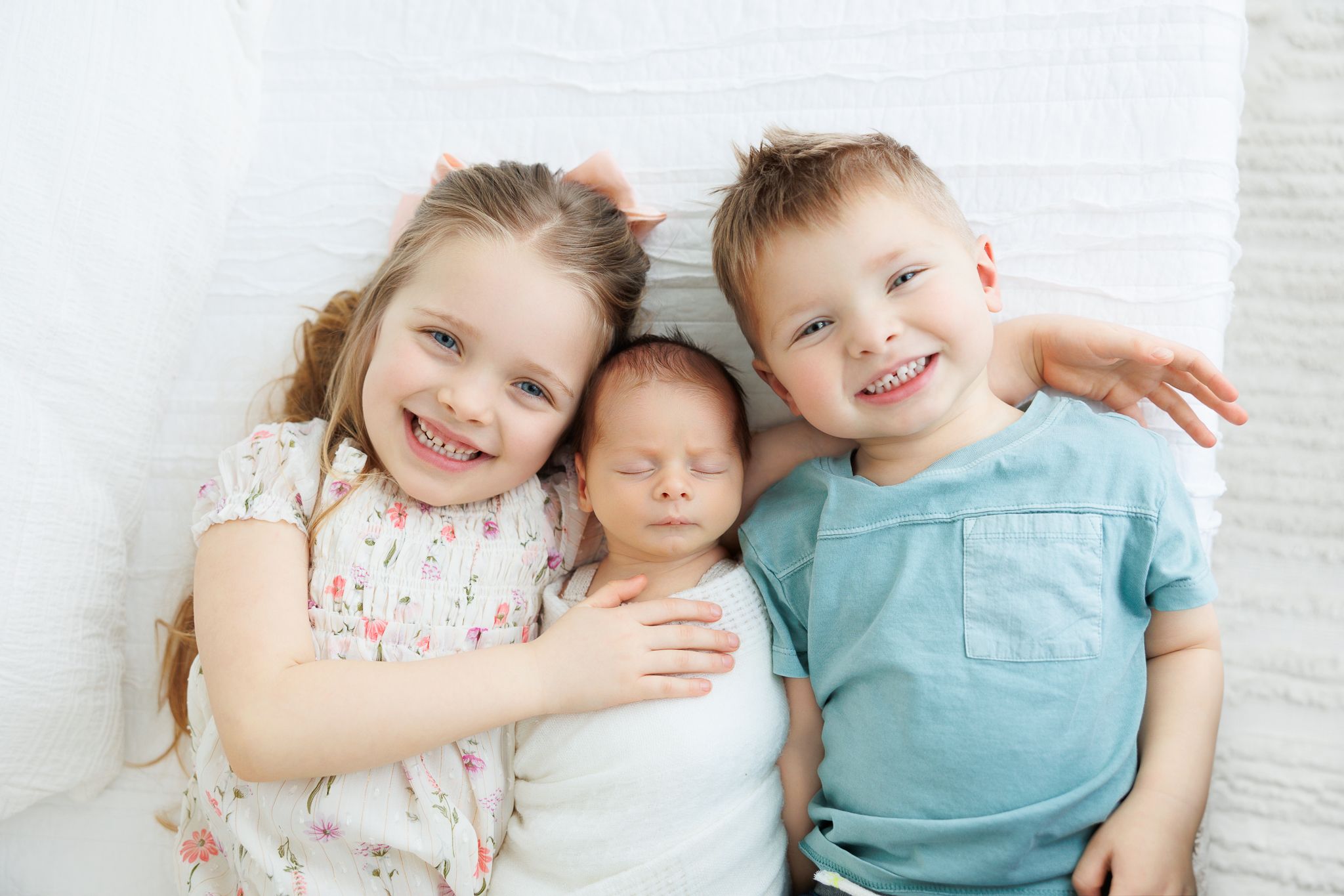 Two young children sitting close together on white background while wearing casual clothing and sharing a sweet moment.