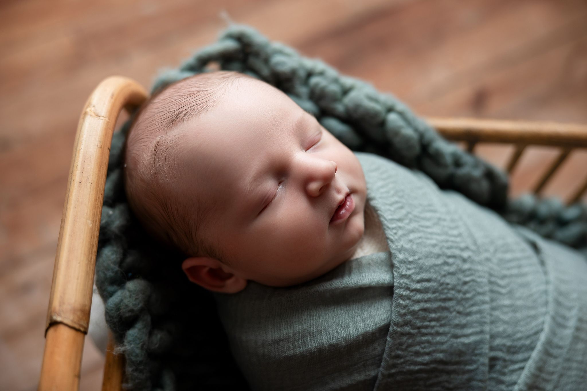Peaceful sleeping newborn wrapped in mint green swaddle rests in vintage wooden chair.
