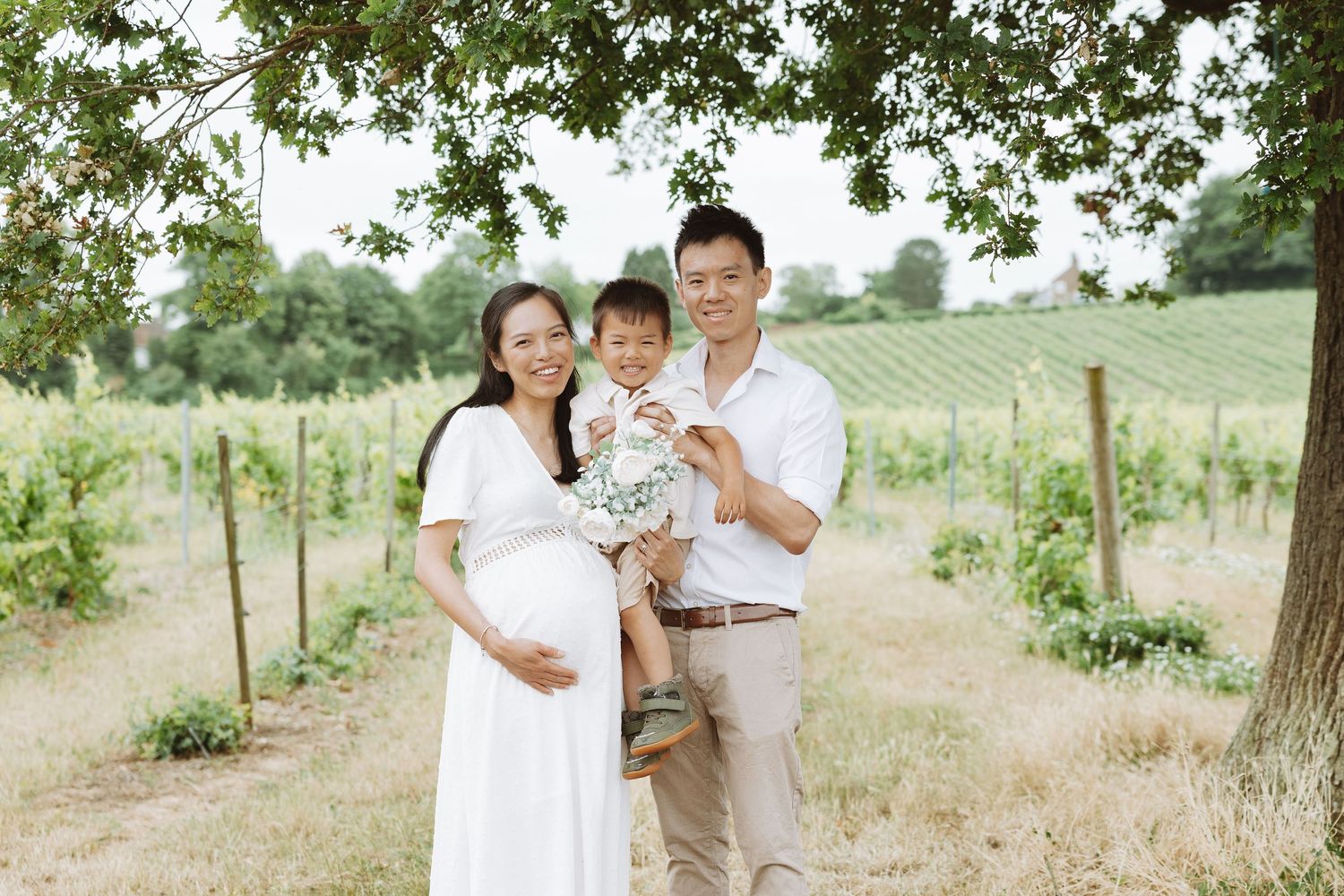 Family in white outfits poses together in a sunlit outdoor setting during an intimate photo session.