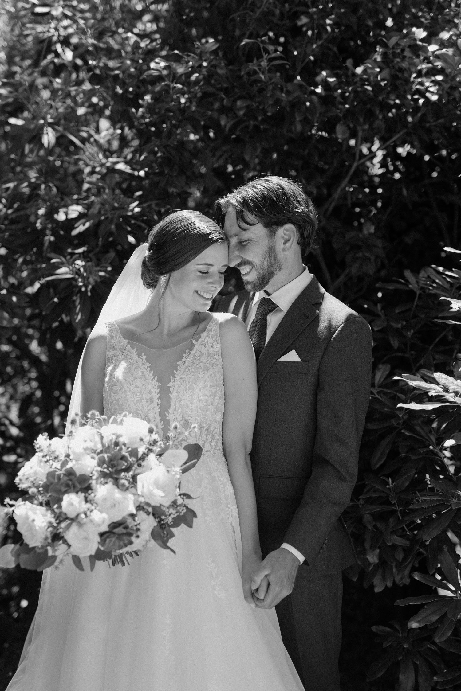 Wedding couple stands under rustic wooden pergola with climbing vines against beige stucco winery building.
