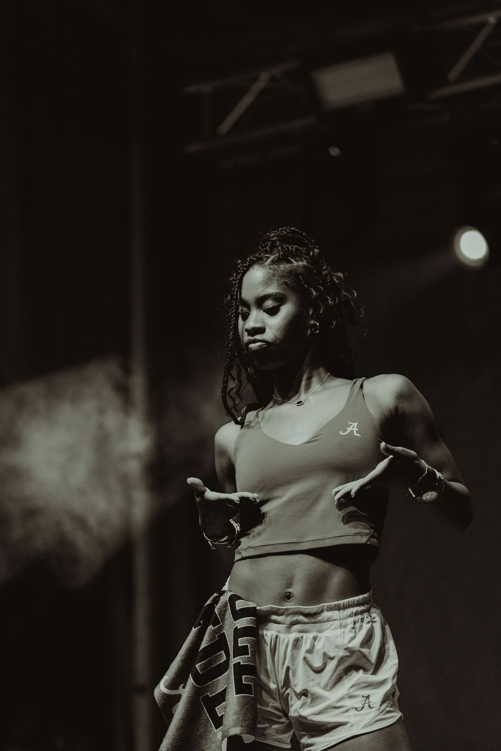 A monochrome portrait of a dancer performing on stage in athletic attire with dramatic lighting and smoke effects.