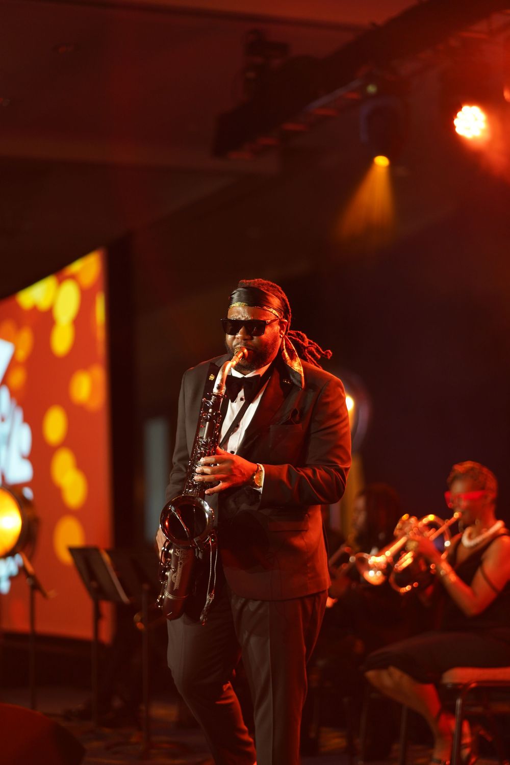 Live performance on stage highlighting musicians in dramatic red lighting performing music with instruments and microphones.
