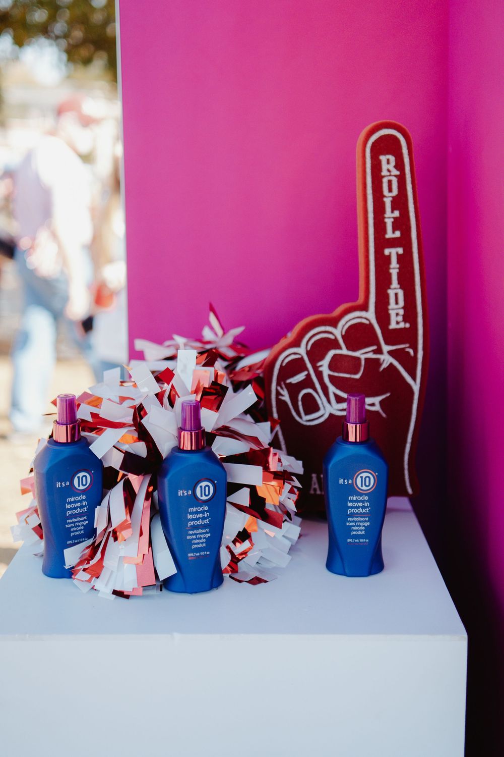Blue beauty product bottles arranged with red and white decorative foam fingers against a vibrant pink background.