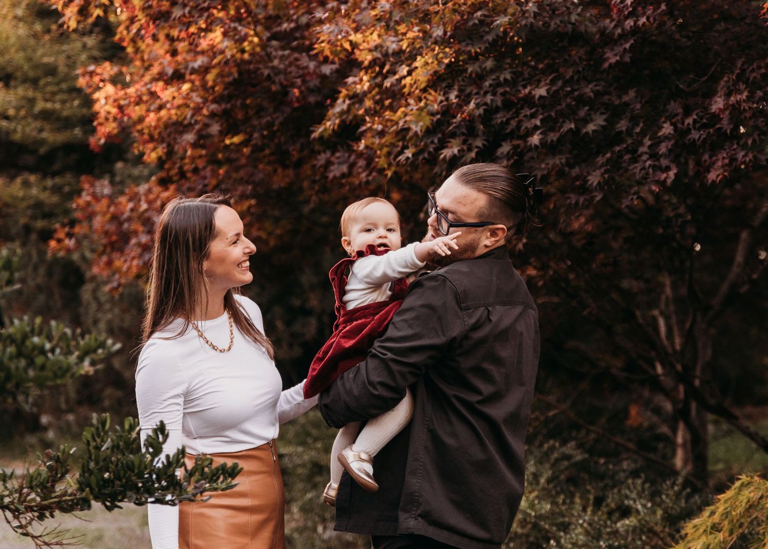 Fall family photoshoot outdoors with autumn foliage and trees in the background during golden hour.