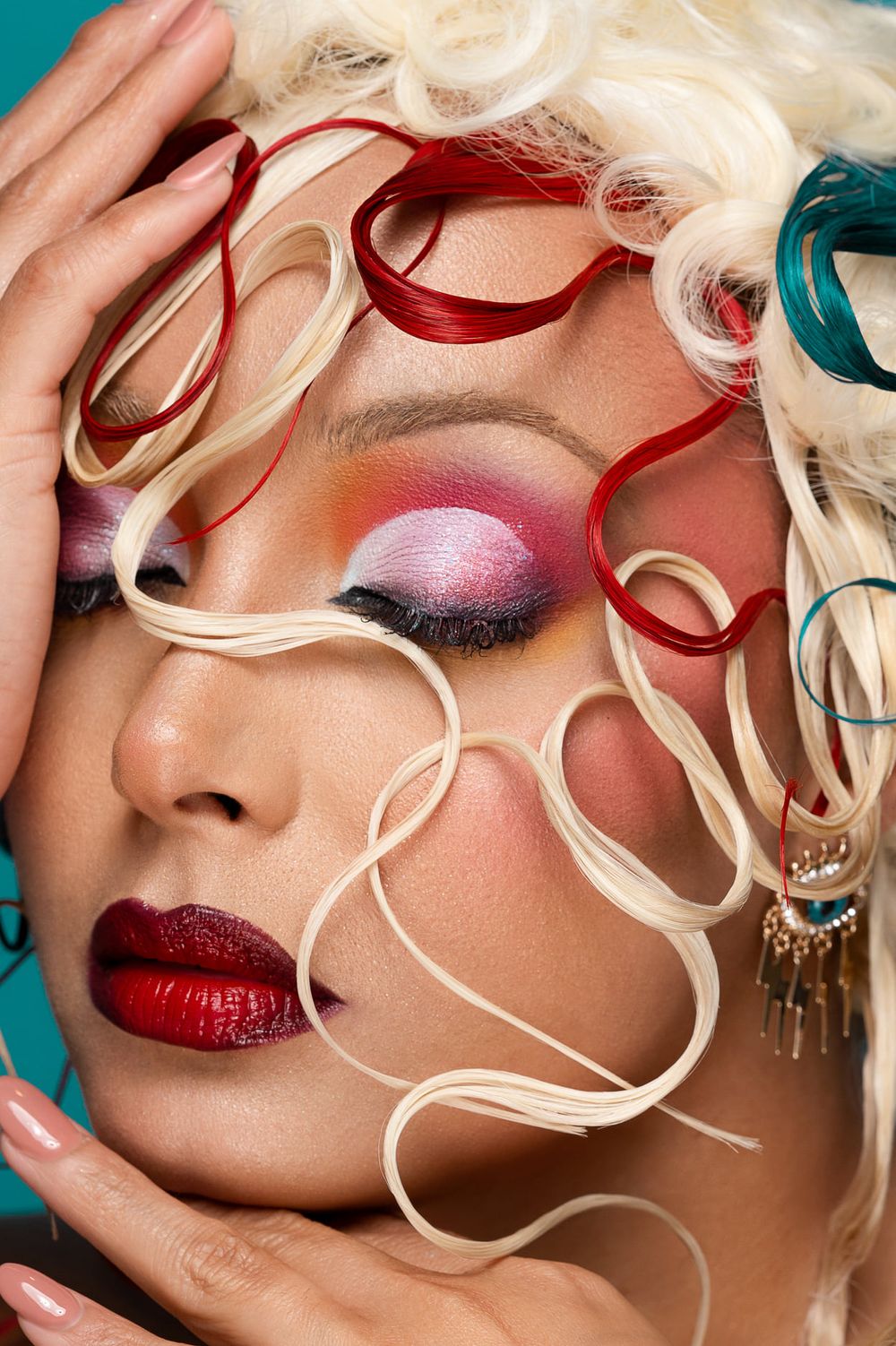 Close-up beauty shot showcasing vibrant pink eyeshadow, red lips, and curled white and red ribbons framing the face.