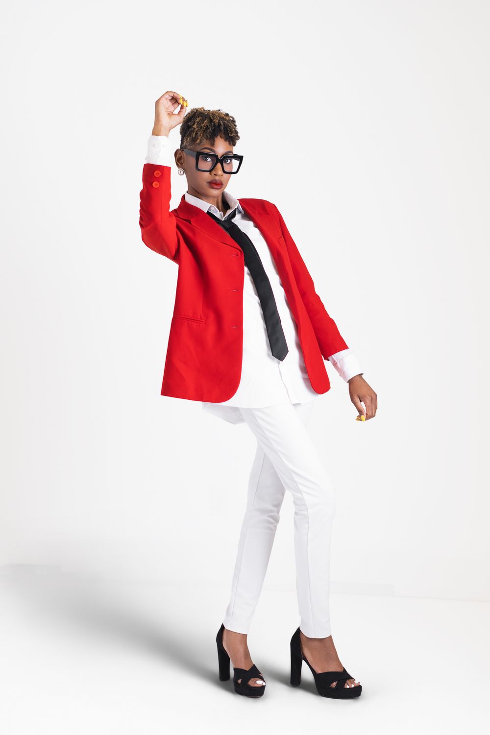 Figure in a striking red blazer and white pants strikes a dynamic pose against white background with raised arm.