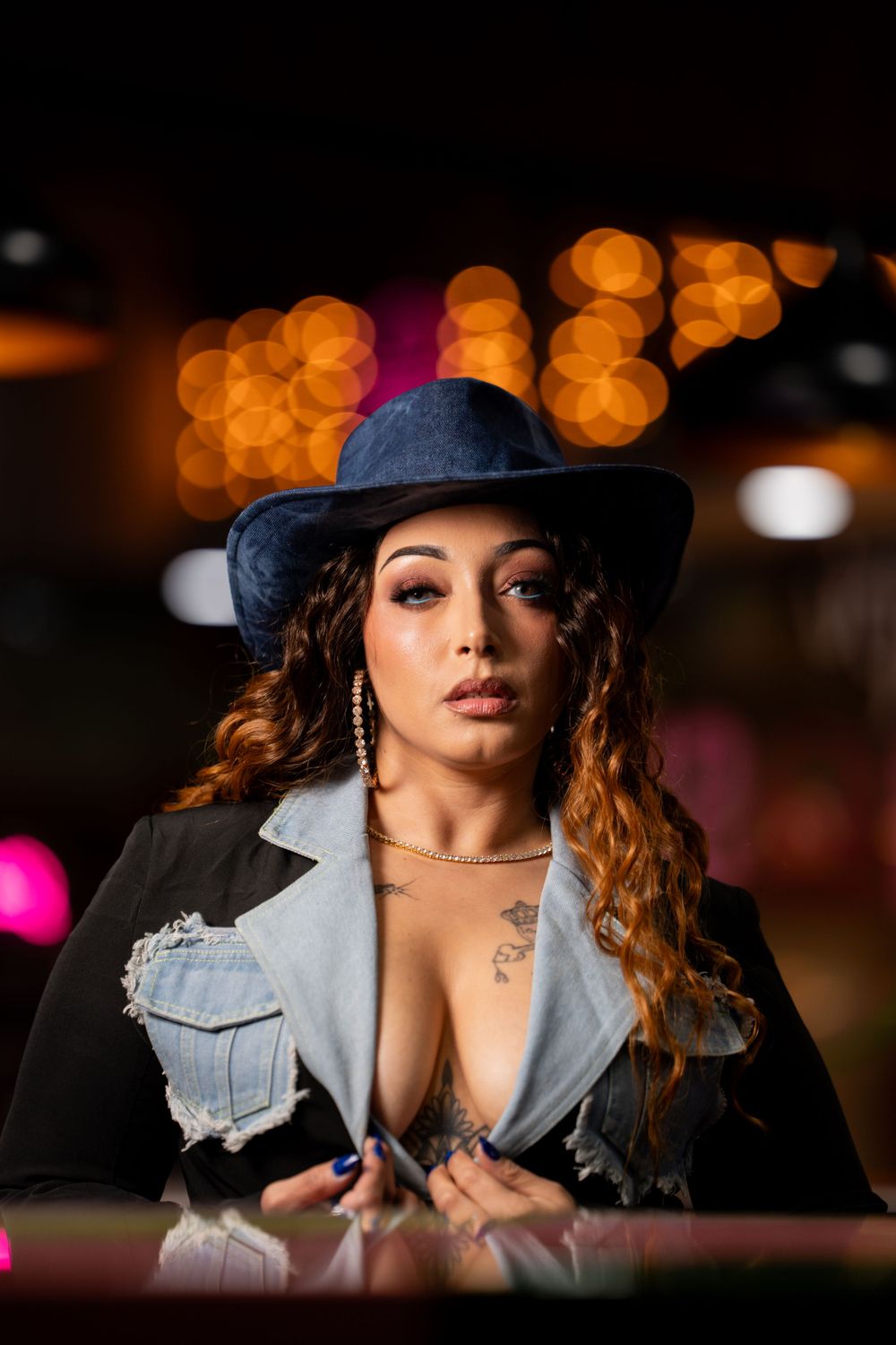 Portrait of model wearing denim jacket and western hat with glowing orange bokeh lights in background.