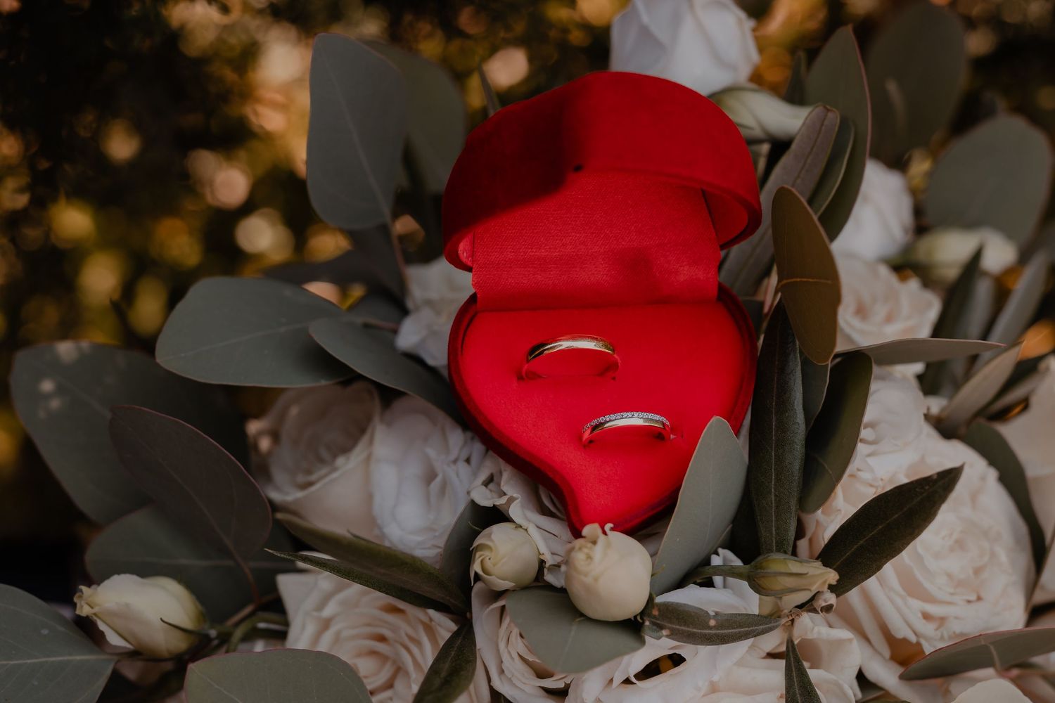 Wedding rings displayed on red and white floral arrangement with moody lighting.