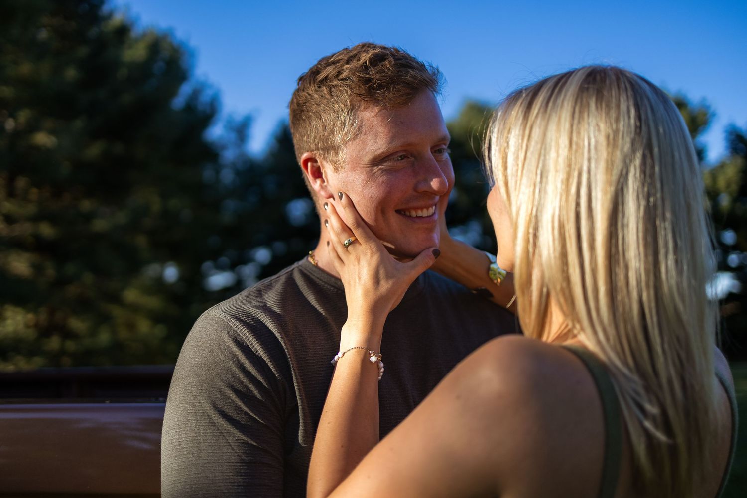 A couple shares an intimate moment while standing in a sunlit meadow field during golden hour.