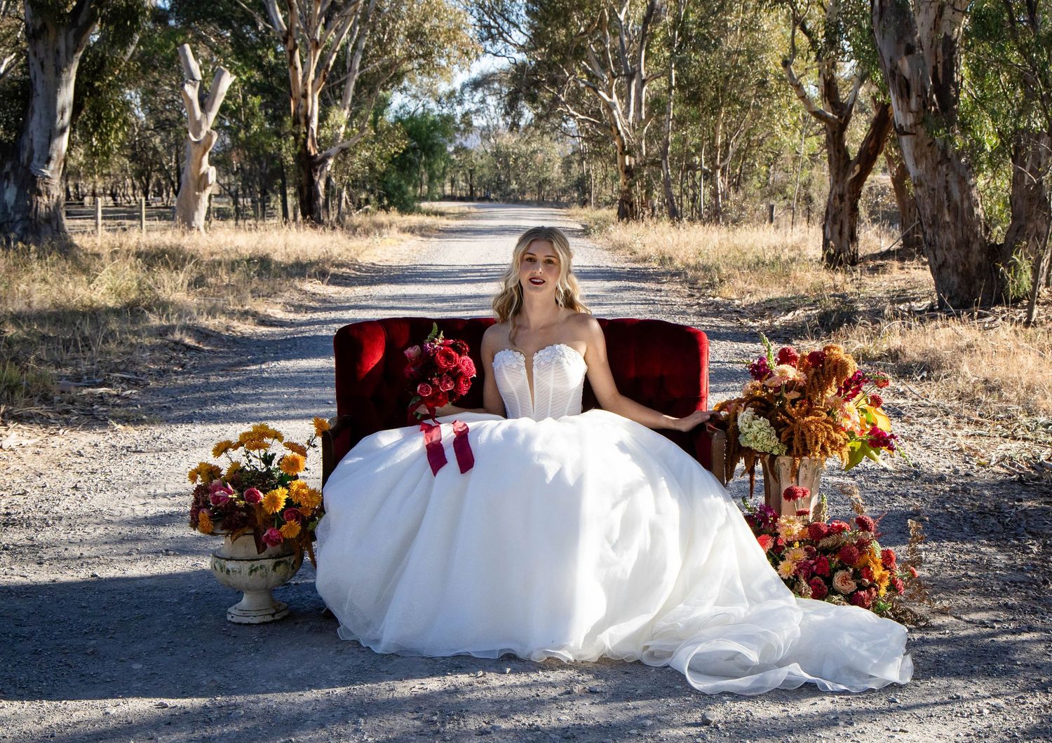 White wedding dress flowing on a rustic dirt path surrounded by autumn colors.
