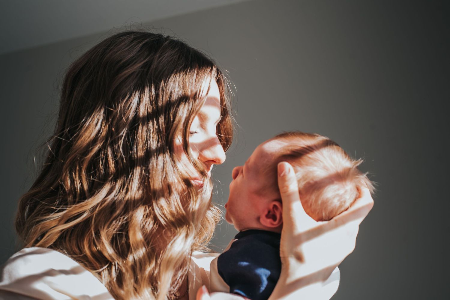 A parent holds and gazes at their newborn baby in warm lighting against a neutral background.