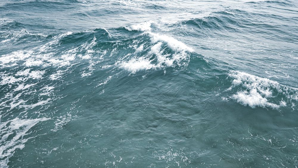 Aerial view of deep blue ocean waves with white foam crests moving across turbulent seawater.