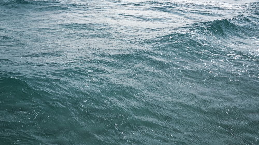 Aerial view of deep blue ocean waves rippling across turquoise waters on a calm day at sea.