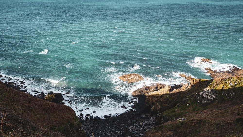 Aerial view of rugged coastline with turquoise ocean waves crashing against rocky brown cliffs.