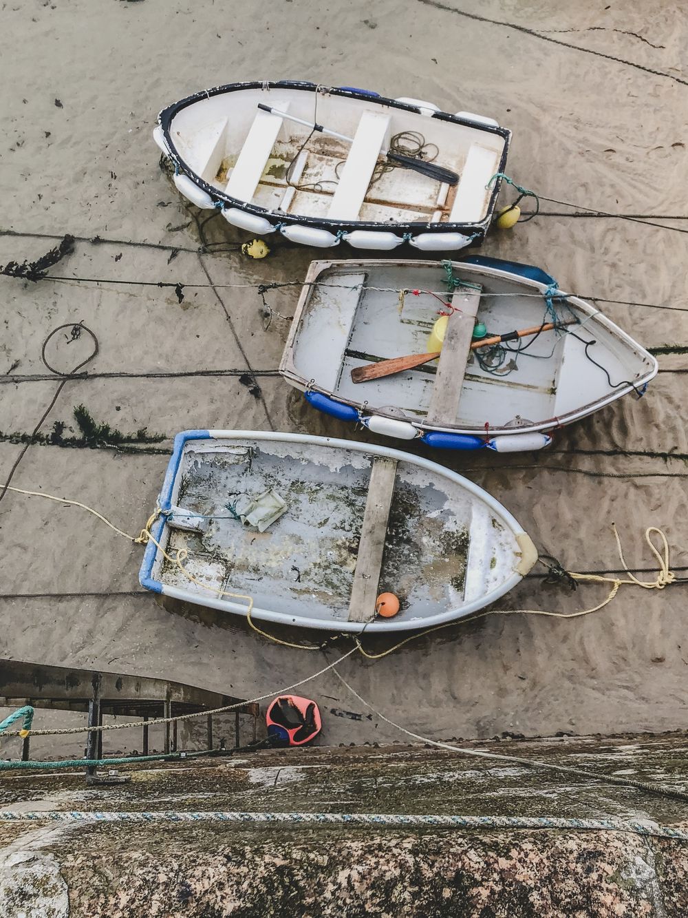 Three white wooden fishing boats sit on exposed sand during low tide with ropes and moorings visible.
