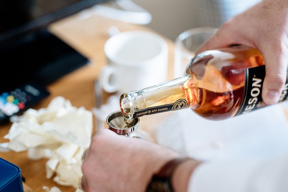 Someone pours rosé wine into a glass on a table with white dishes in the background.