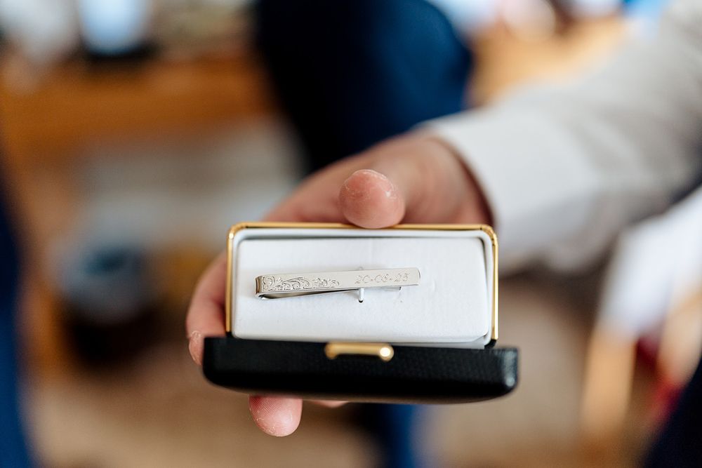 A hand holds a small black case containing what appears to be a silver pin or brooch on white cushioning.