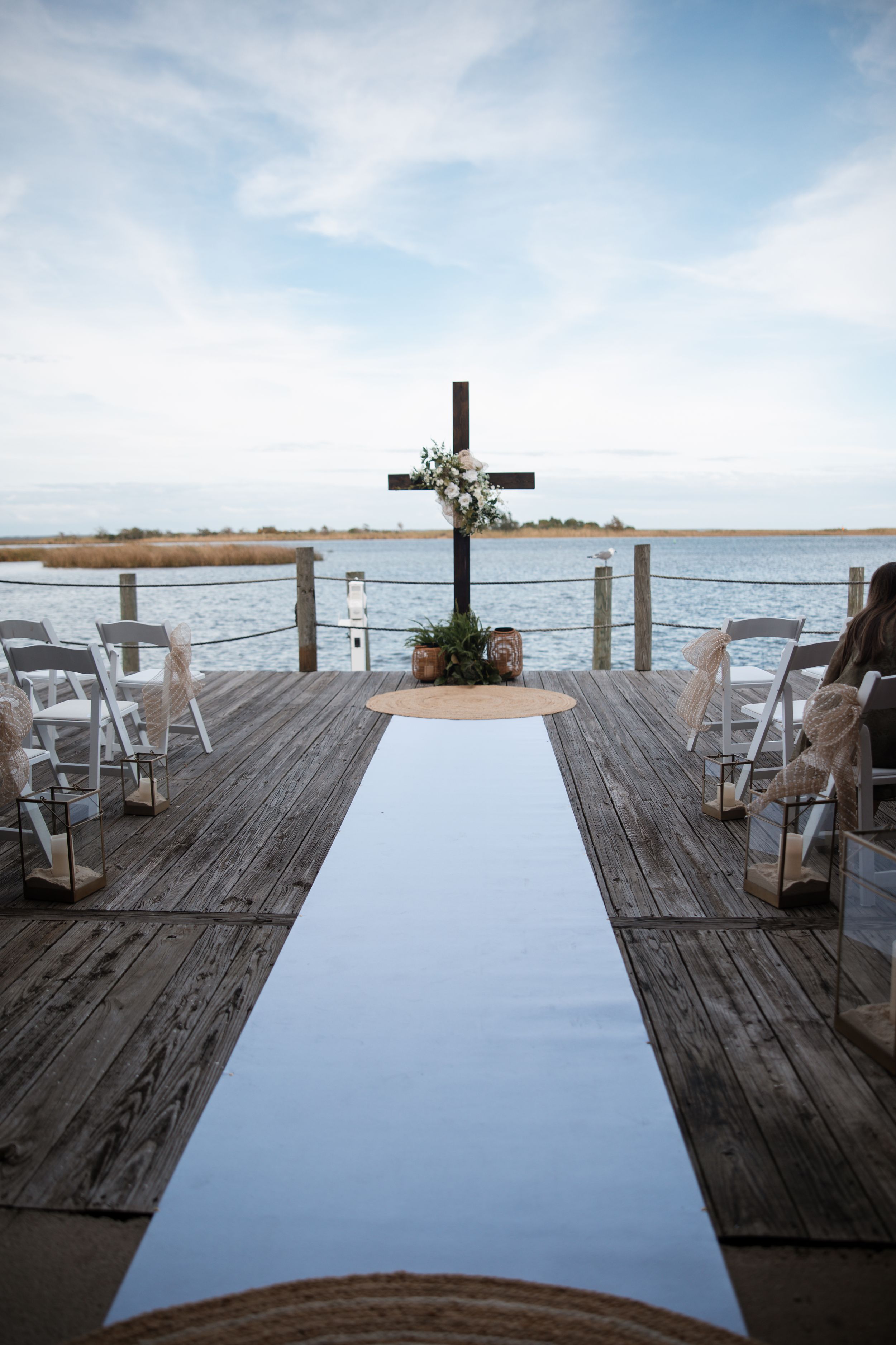 Sequence of dock photos showing setup for a waterfront wedding ceremony with white chairs, cross, and scenic ocean views.
