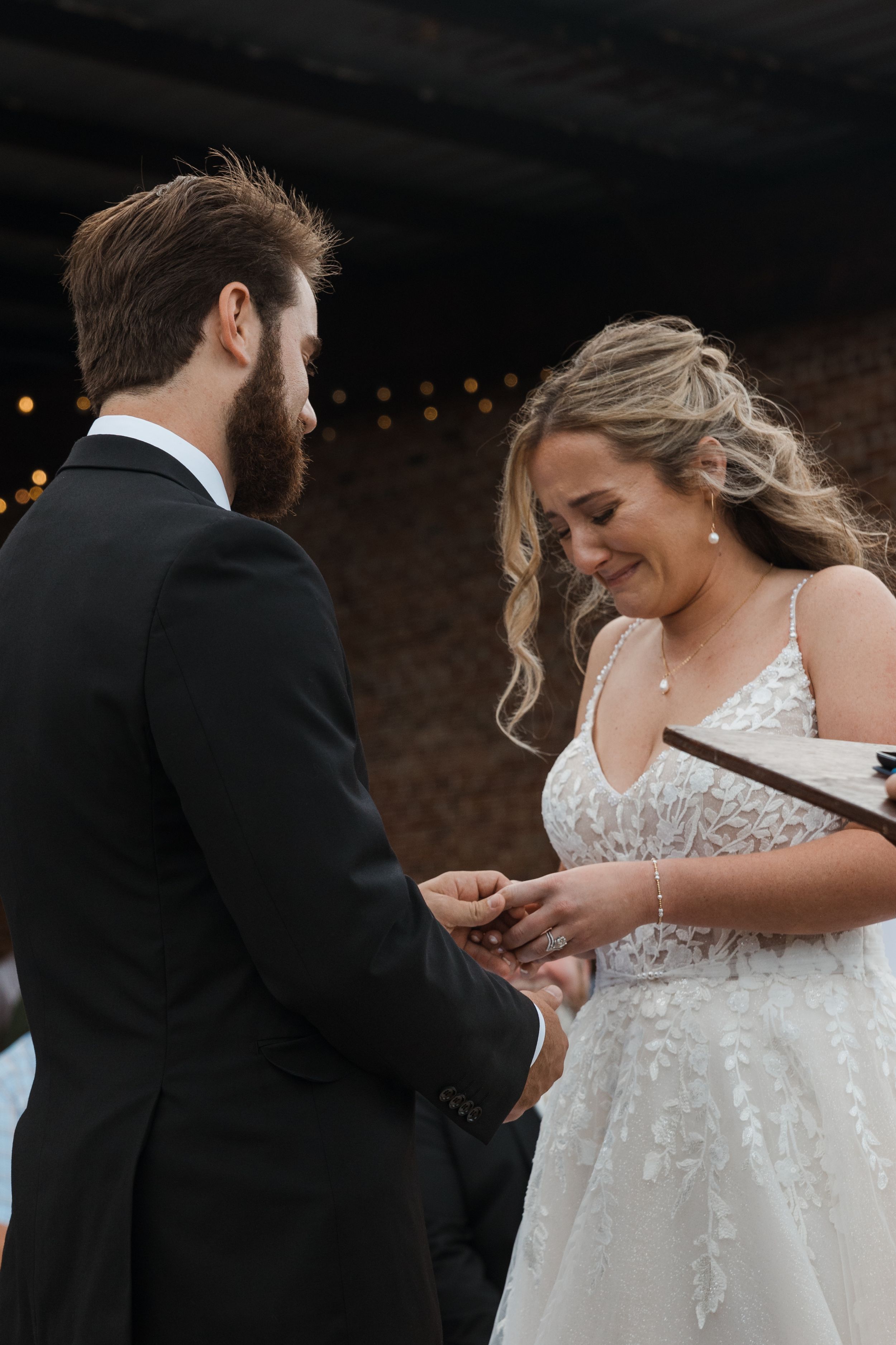 A couple exchanges rings during an intimate wedding ceremony under romantic mood lighting.
