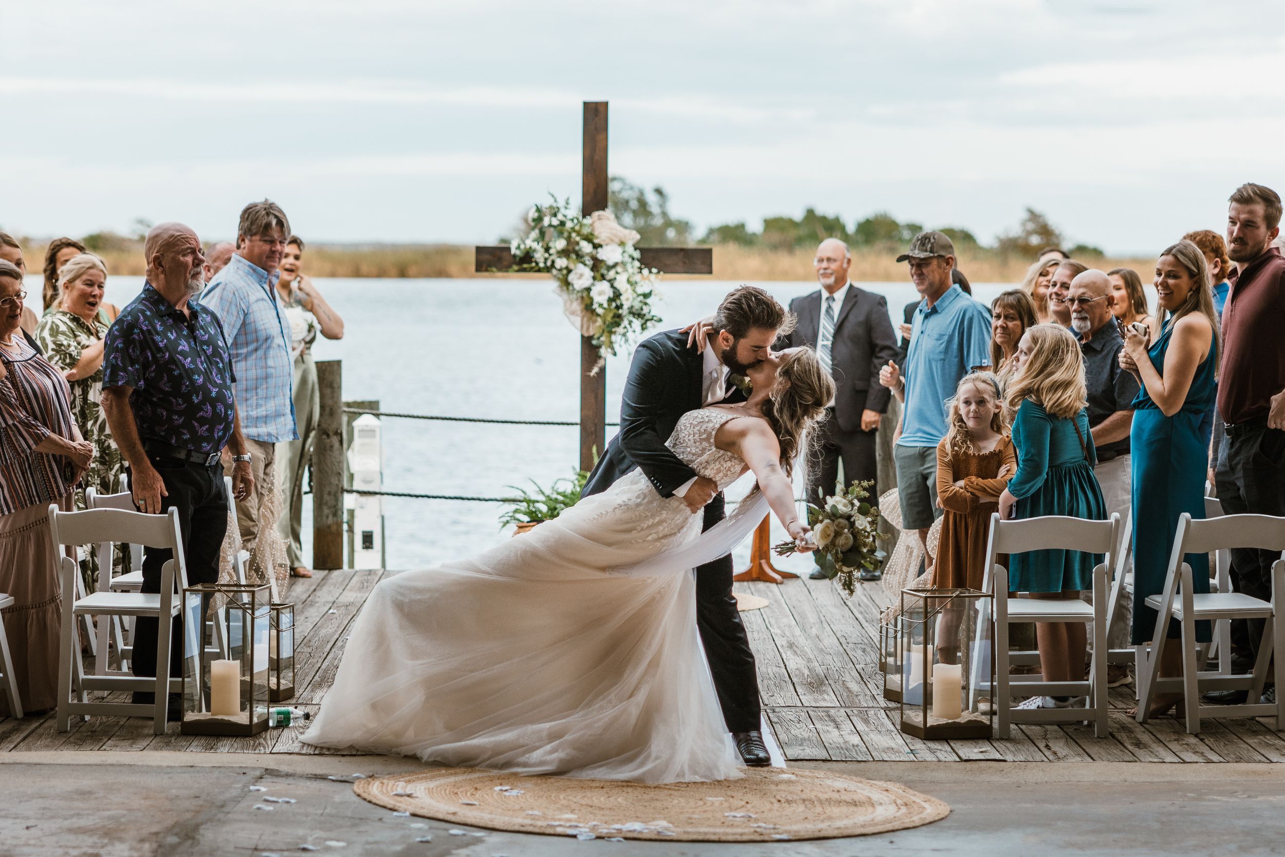Wedding guests dance and celebrate under twinkling lights at an outdoor evening waterfront reception.