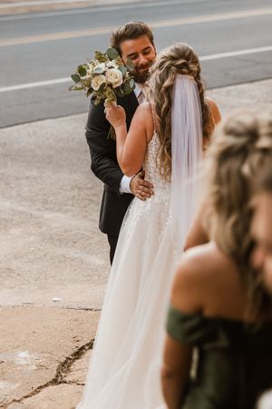 An intimate wedding moment captured outdoors with the couple embracing against a soft blurred background.