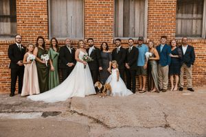 A wedding party group photo taken outside a rustic brick building venue.