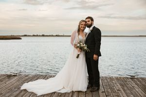 Newlyweds share a romantic moment on a wooden dock overlooking a serene waterfront at sunset.