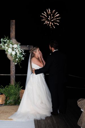 A couple shares a romantic moment under fireworks display during their outdoor nighttime wedding ceremony.