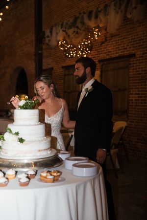 A couple cuts their elegant white wedding cake at their rustic brick-walled reception venue.