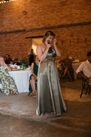 Bridesmaids in sage green dresses having fun dancing and spinning on a rustic brick venue dance floor at a wedding reception.