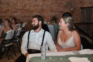 Wedding guests seated at tables listen intently during reception speeches in rustic brick venue.