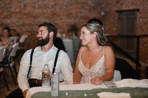 Newlyweds share a relaxed moment at their reception table inside a rustic brick-walled venue.