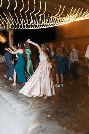 A festive wedding reception dance floor with people dancing under string lights while someone in a pink dress twirls.