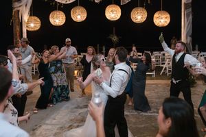Wedding guests dance and celebrate on a rustic dance floor under glowing spherical lantern lights at an evening reception.