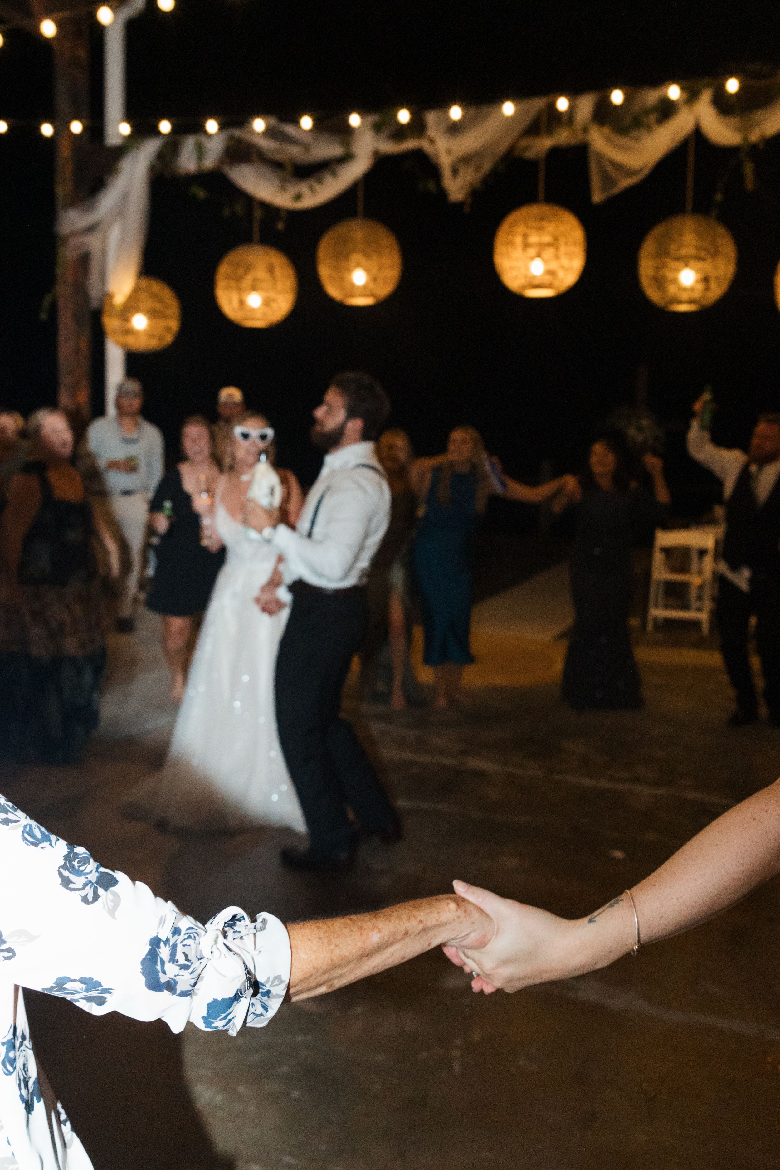 Wedding guests dancing under glowing paper lanterns at an evening reception with romantic lighting.