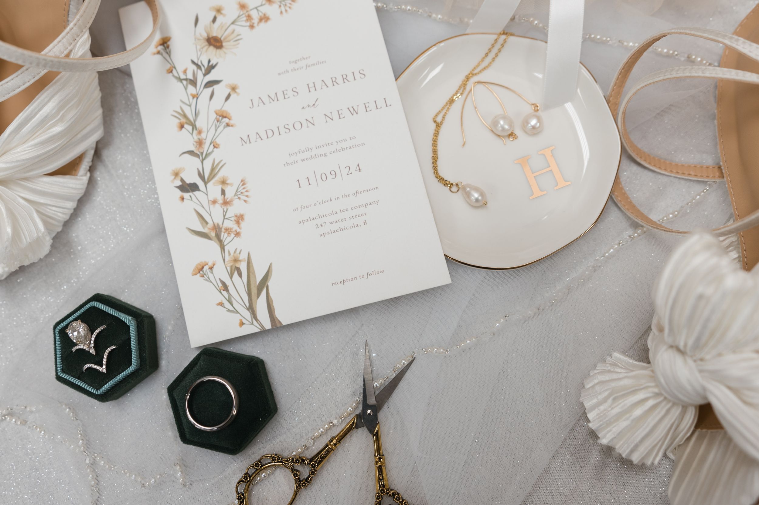 Elegant wedding invitation with gold floral design displayed alongside ring boxes, scissors and decorative elements.