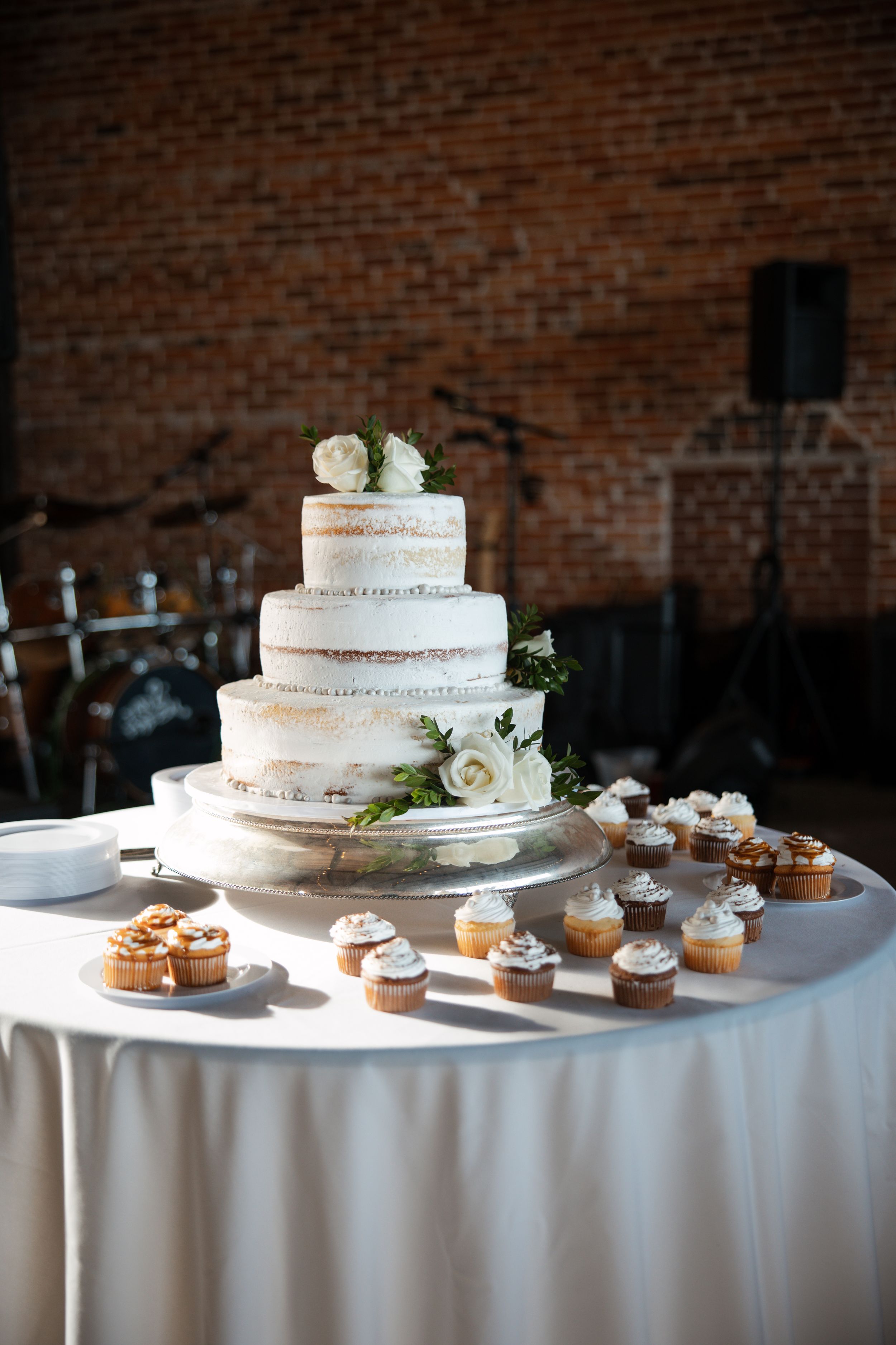 A wedding dessert display with multiple tiers of white naked cakes and cupcakes arranged on white tablecloths.