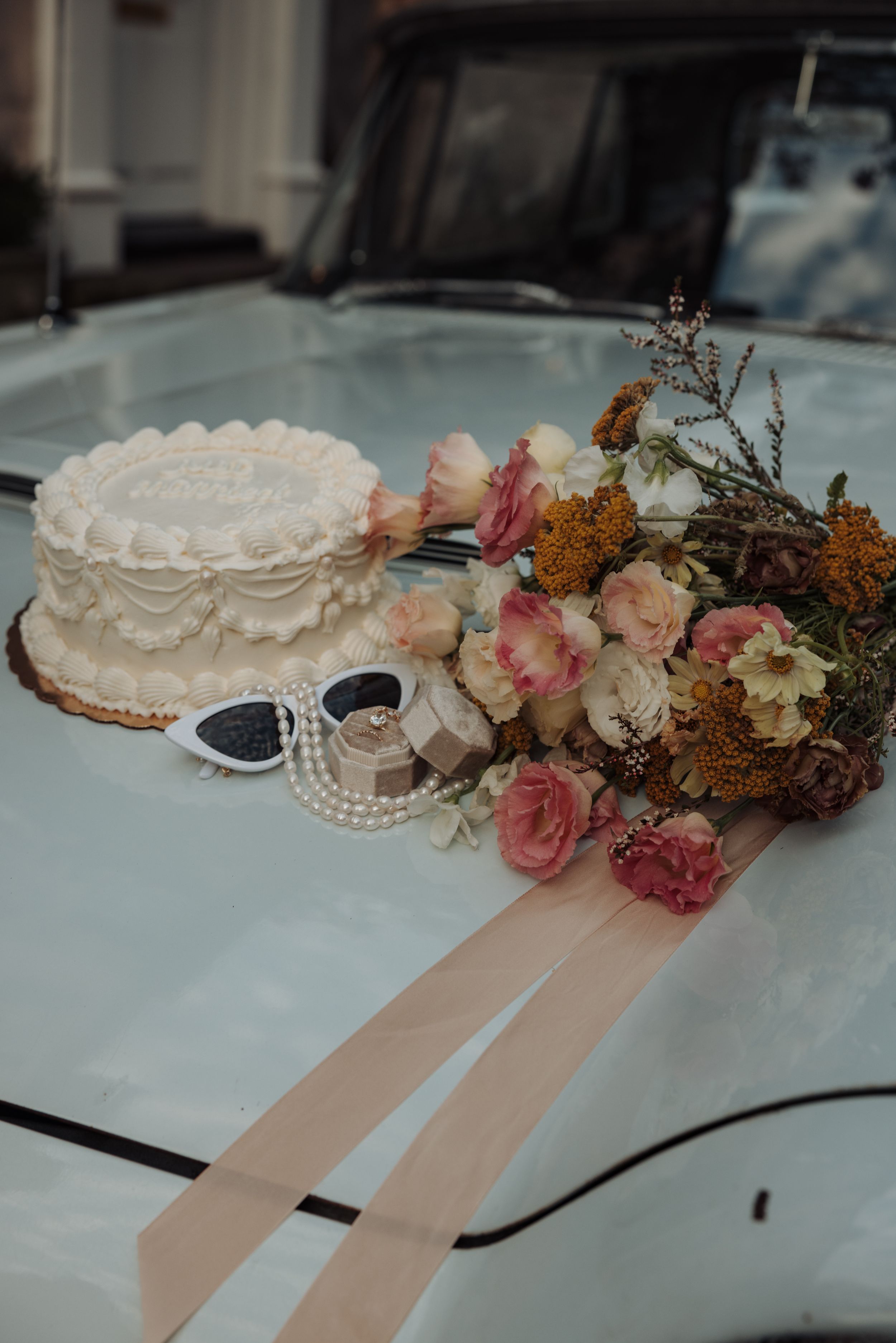 Wedding cake decorated with delicate lace patterns and blush pink flowers with trailing peach ribbons.