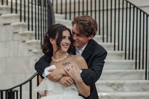 A romantic wedding couple embraces lovingly on stone steps with an iron railing in the background.
